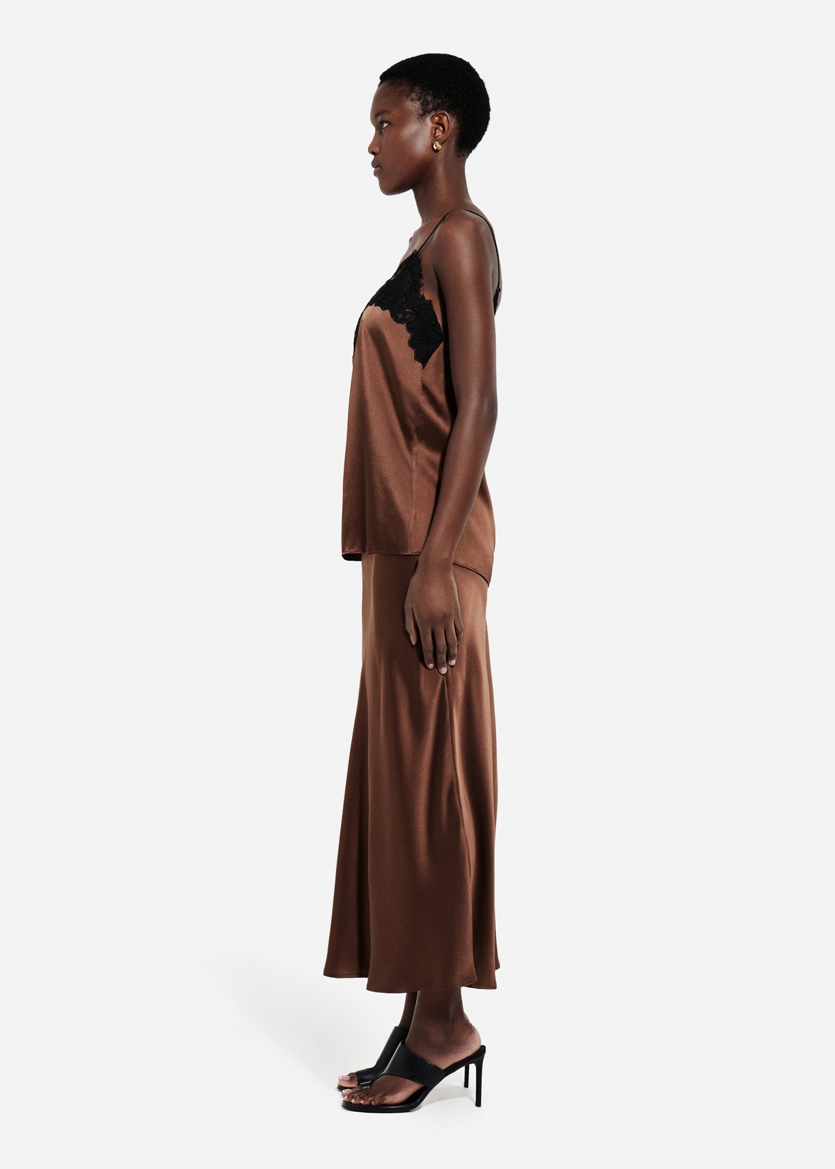 Bias Cut Slip Skirt in Silk - Chocolate, Woman wearing a brown satin skirt and cami with black lace details on a white background side, image 2 of 4